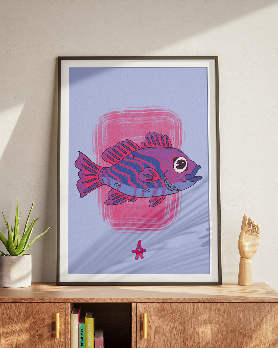 Framed artwork of a purple fish on a light wall above a wooden cabinet.