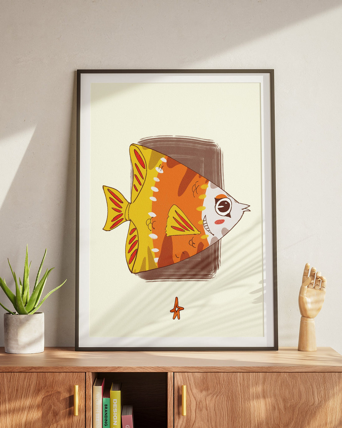Framed artwork of a colorful fish on a wooden cabinet with a plant and small sculpture.