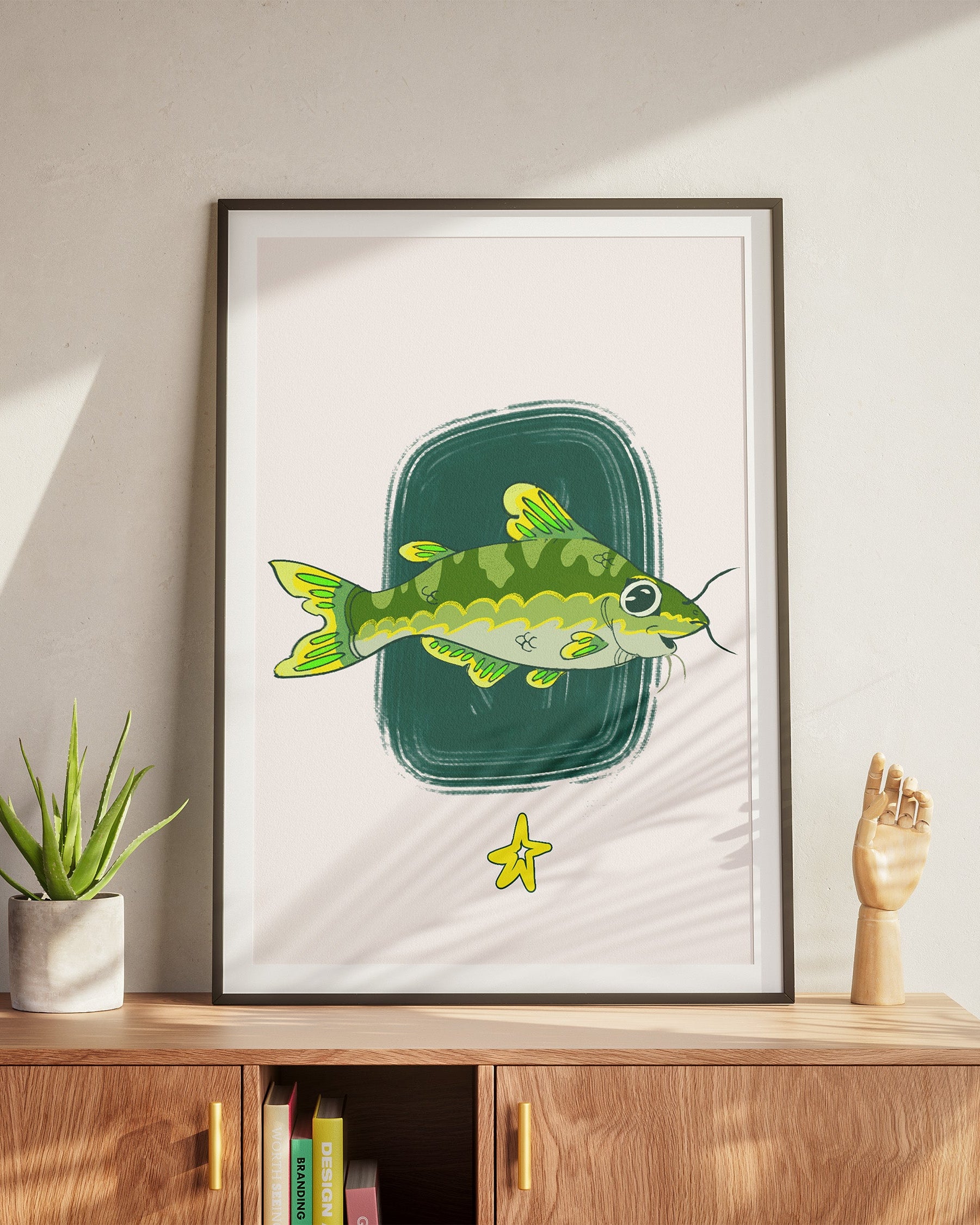 Framed artwork of a green fish on a white background, displayed on a wooden cabinet.