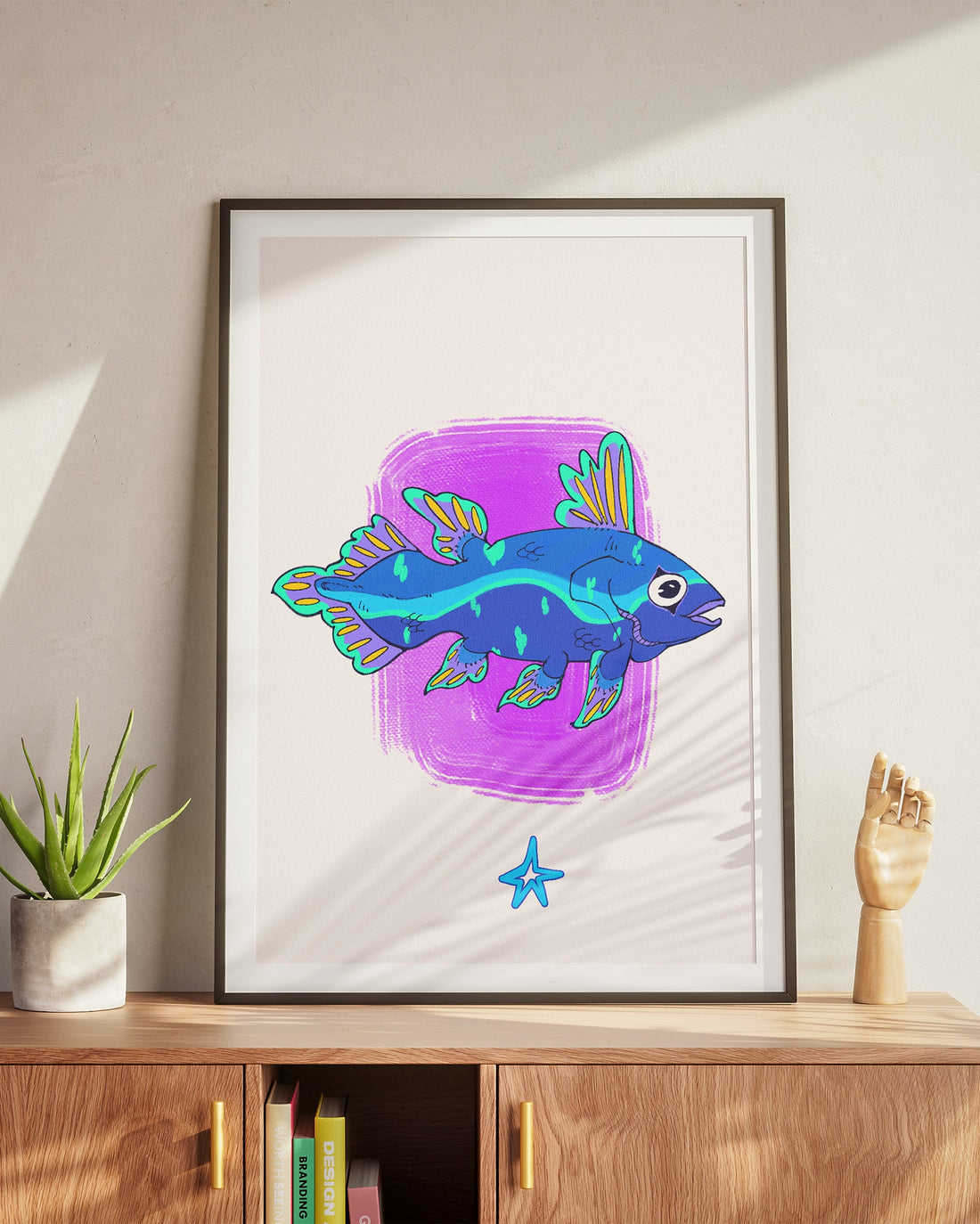 Framed artwork of a blue fish with purple background on a wooden cabinet.