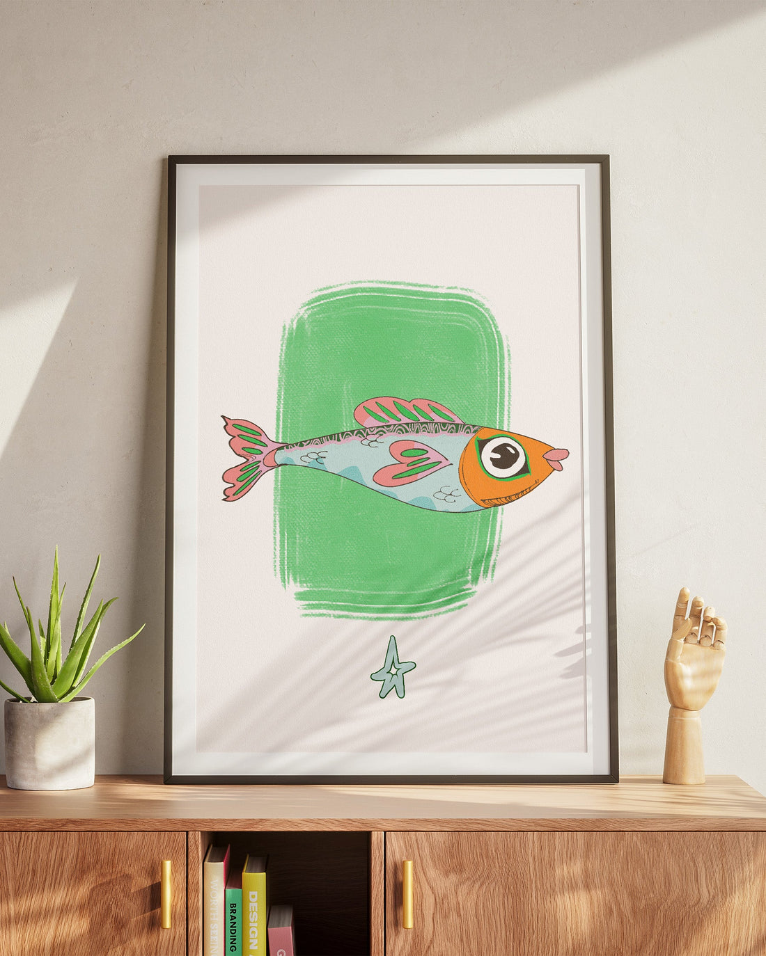 Framed artwork of a colorful fish on a wall above a wooden cabinet.
