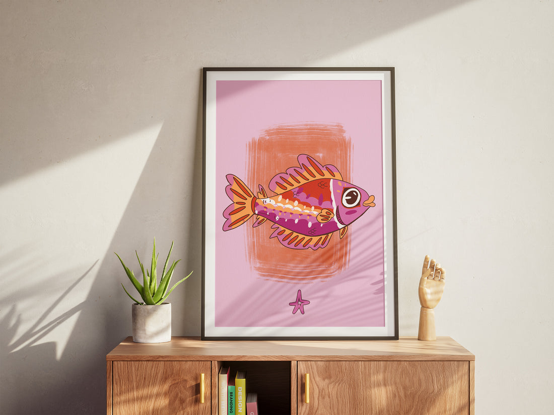 Framed artwork of a colorful fish on a pink background, displayed on a wooden cabinet.