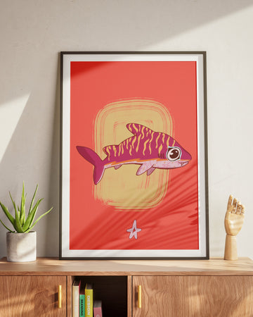 Framed artwork of a fish on a red background in a room with a wooden cabinet and plant.