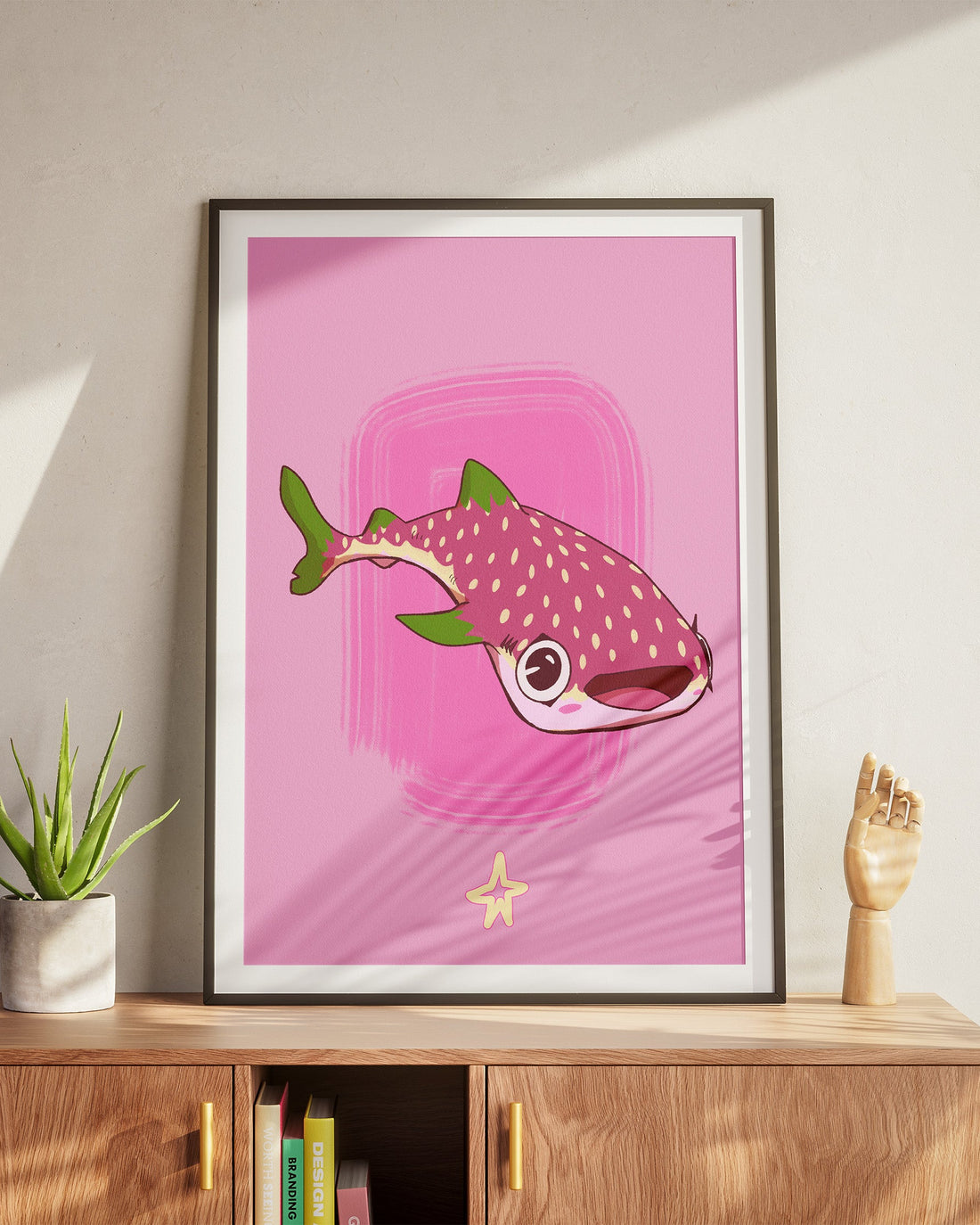 Framed artwork of a fish on a pink background on a wooden cabinet.