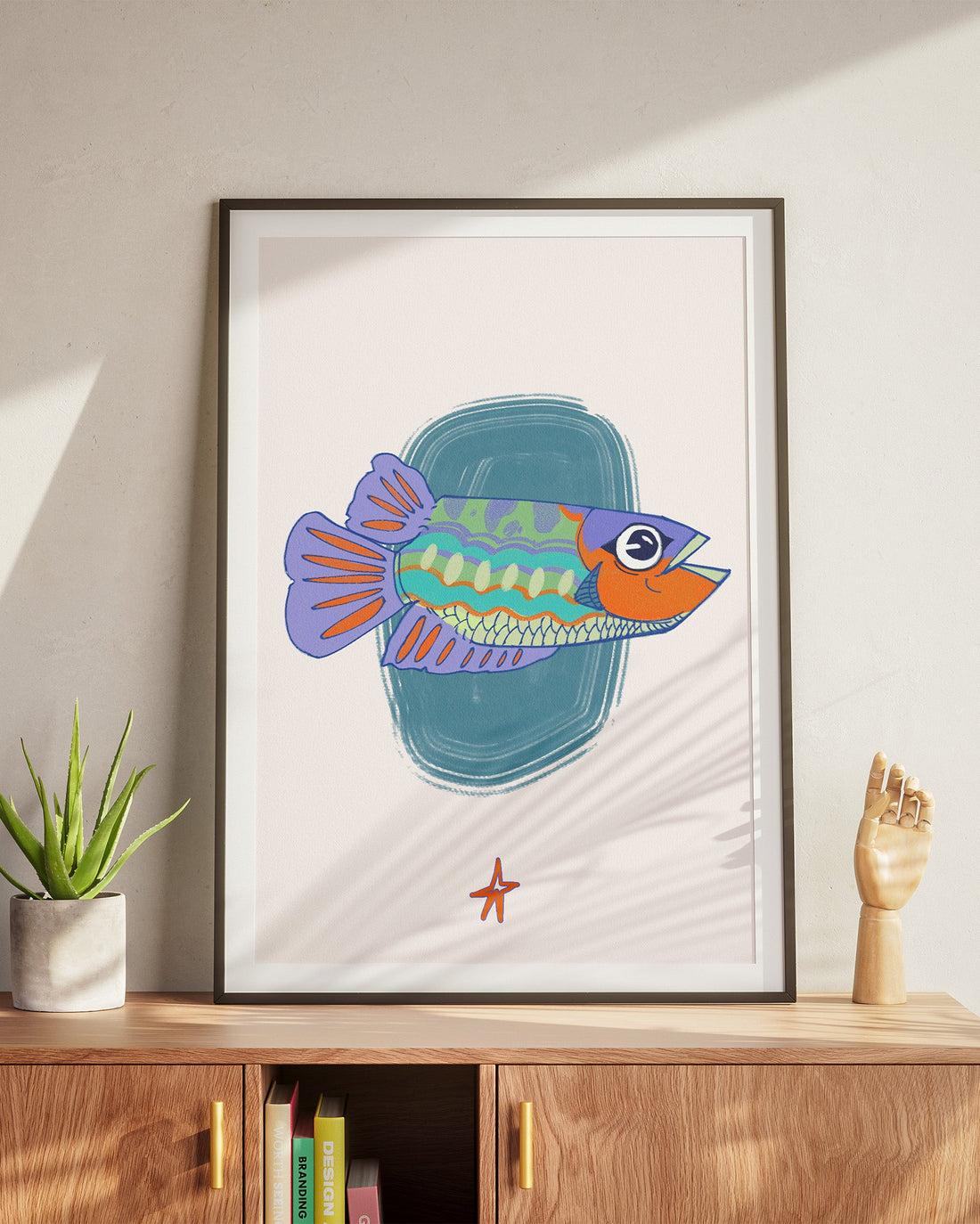 Framed illustration of a colorful fish on a wall above a wooden cabinet.